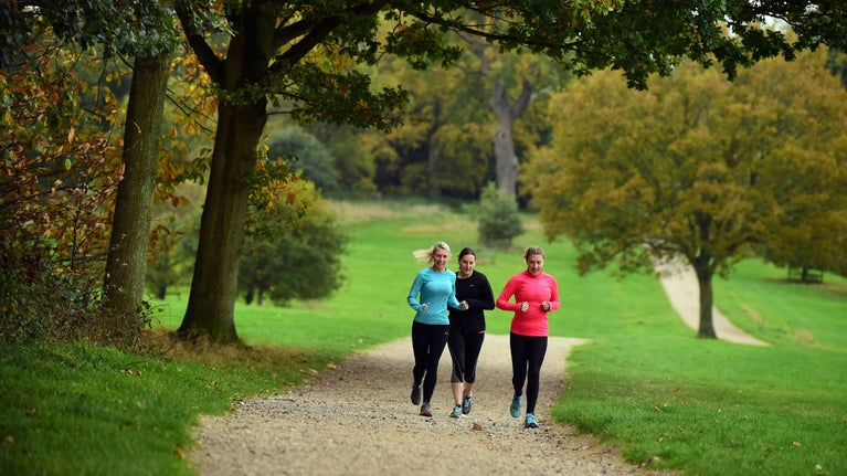 Three female runners running along a track through parkland towards the camera